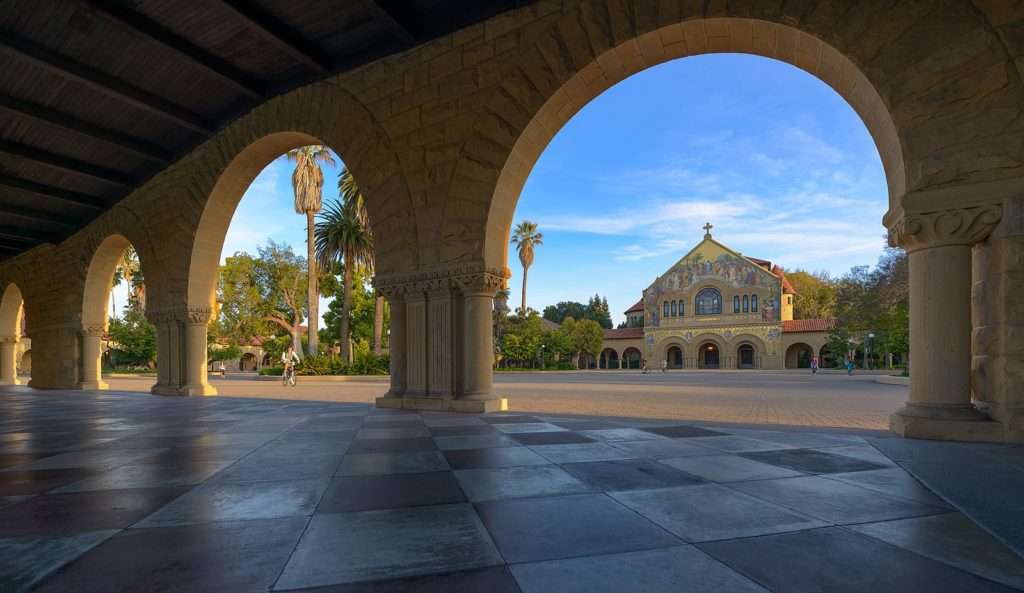 A church featuring a mural sits beyond rounded arches at Stanford University.