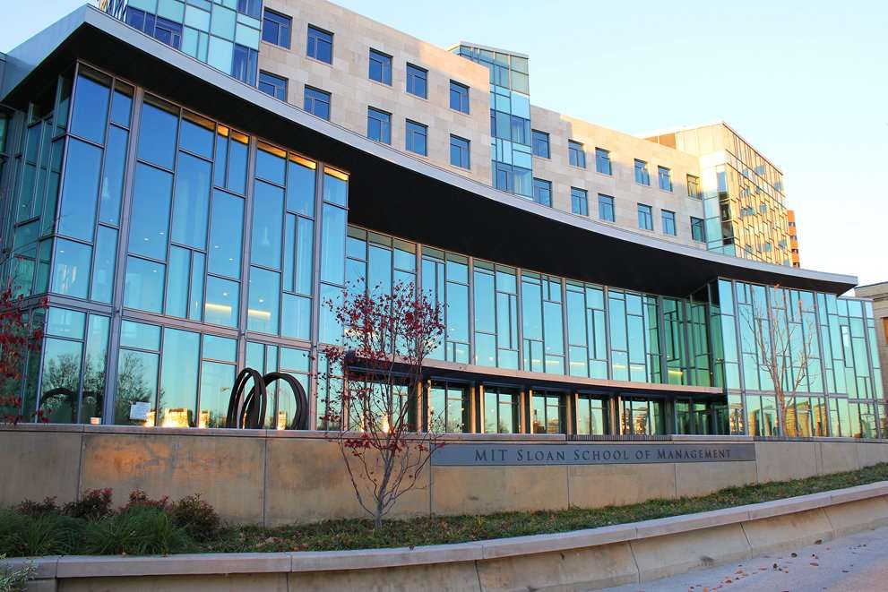 The glass facade of MIT’s Sloan School building is featured.